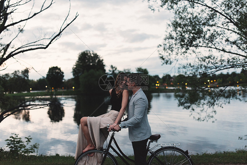 吉卜赛年轻夫妇骑自行车在黄昏的湖边互相看望着对方图片
