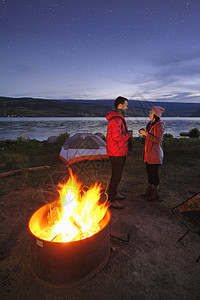 几人站在帐篷和营火附近在黄昏喝热饮图片