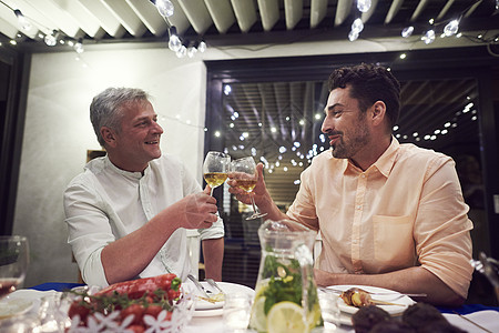 两个男人坐在晚餐桌边拿着红酒杯做吐司图片