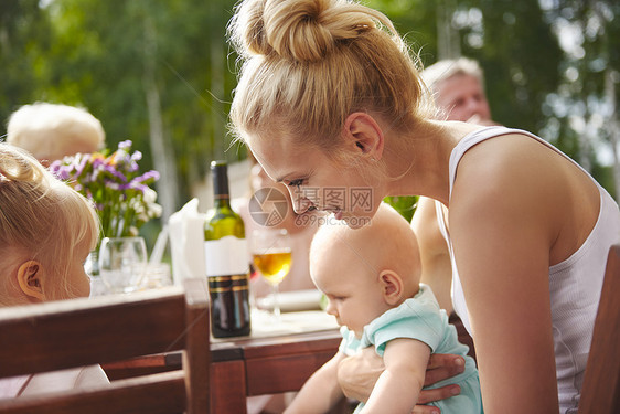 带着婴儿和幼女的年轻青在庭院桌旁吃家用午餐图片