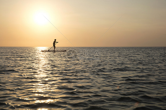 海上日落时在冲浪板上滑行的人图片