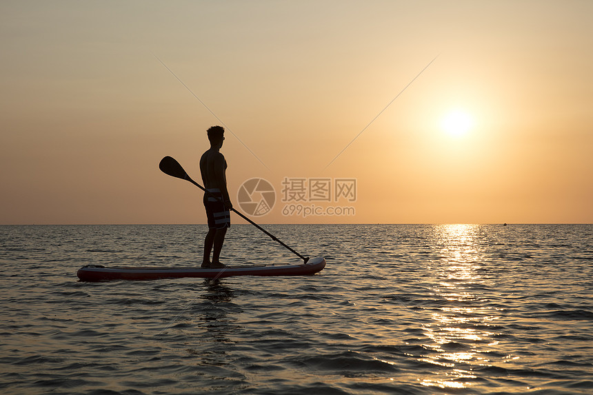 海上日落时在冲浪板上滑行的人图片