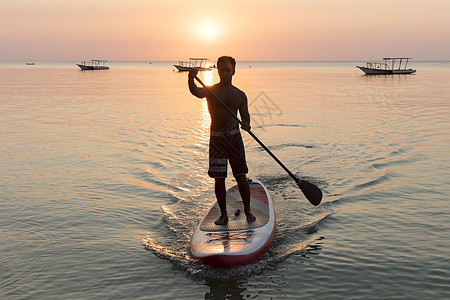 海上日落时在冲浪板上滑行的人图片