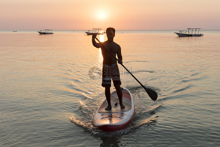 海上日落时在冲浪板上滑行的人图片