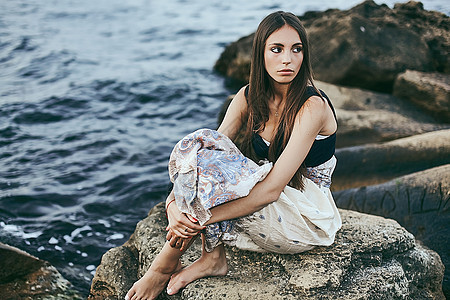 乌克兰敖德萨一名年轻女子坐在海岸岩石上回头看图片