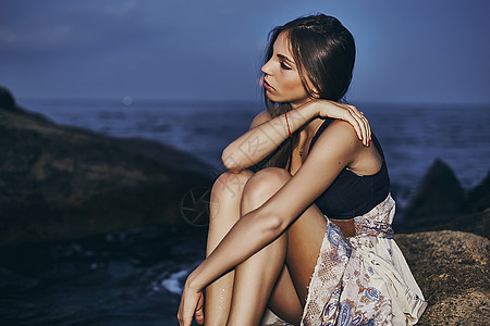 乌克兰敖德萨黄昏时分坐在海岸岩石上的年轻女子图片