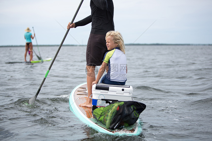 女人和年轻男孩一起坐在桨板上另一只远处的桨板图片