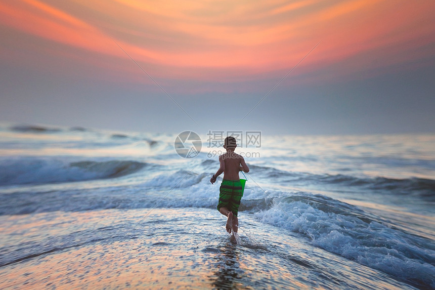 男孩在日落时跑向大海图片