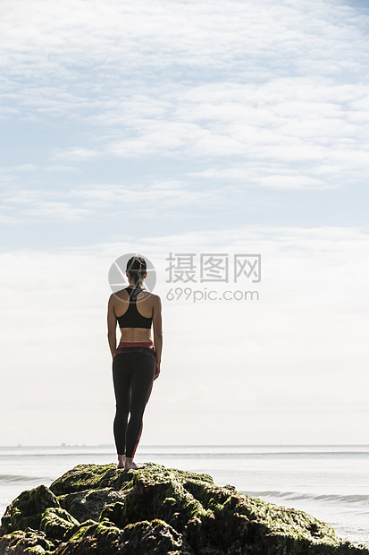 年轻女选手在海滩岩石向远看的背影图片
