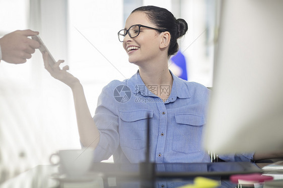 办公桌上的年轻女办公室职员看同事的智能手机图片