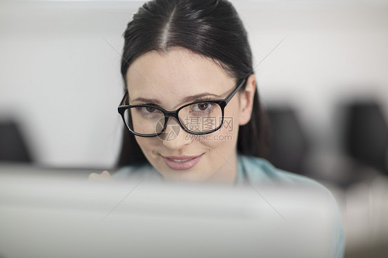 从台式计算机上找的年轻女办公室工作者的肖像图片