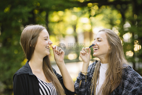 两个年轻女人在公园拿着树叶假扮胡子面对面笑图片