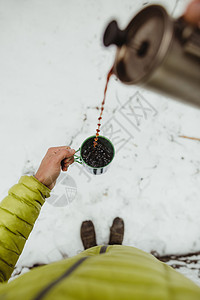 男徒步旅行者站在雪地上倒咖啡的手图片