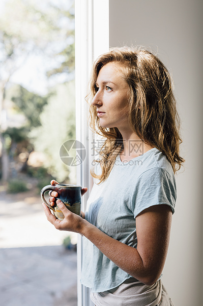 在院子门口拿着咖啡向外看的年轻女子图片