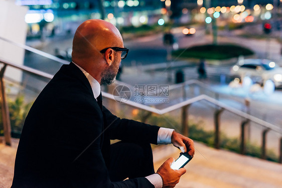 成熟商人夜间户外坐在台阶上手持智能机图片