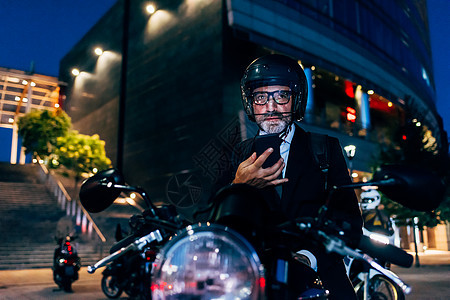 中年男子夜晚在户外坐在摩托车上玩手机图片