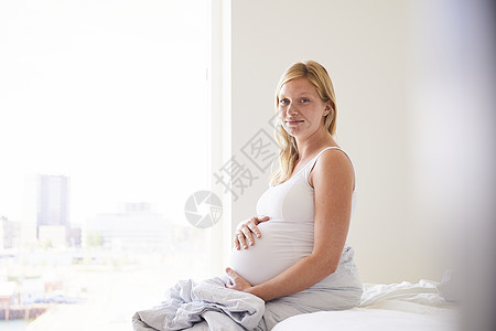 怀孕的年轻妇坐在床上手摸着肚子背景图片