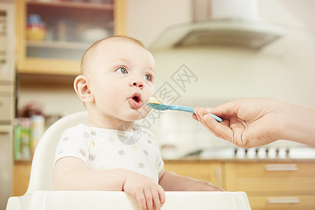 婴儿男孩坐在高椅子上母亲用勺喂食图片