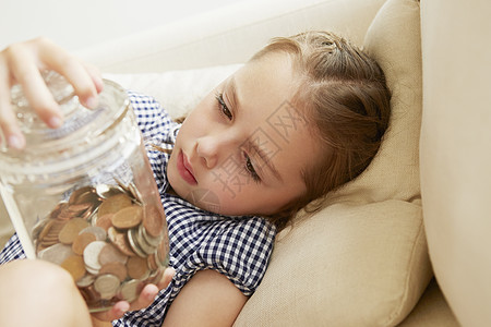 年轻女孩在沙发上拿着一罐钱思考的表情图片