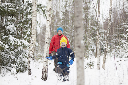 父亲和儿子在被雪覆盖的森林中行走图片