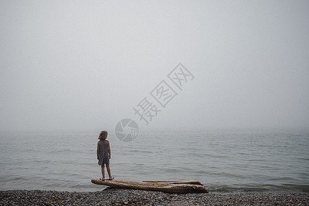 女孩站在漂浮木上看着大海图片