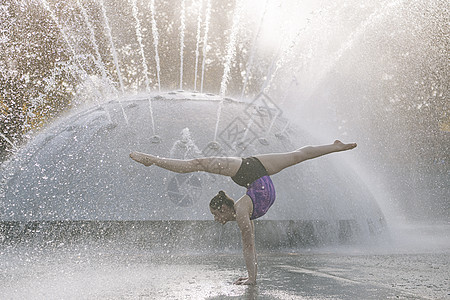 在喷泉旁边的少女摆出瑜伽姿势保持平衡图片