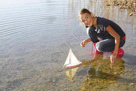 女孩在水上玩漂浮的玩具船图片