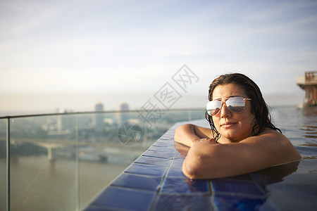 戴太阳眼镜的女子趴在游泳池边曼谷图片