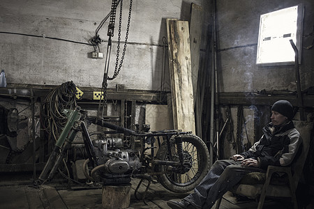 在车间用拆除的老式摩托车在间用手椅抽烟的机械师图片