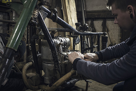 在车间修理旧式摩托车发动机的男人图片