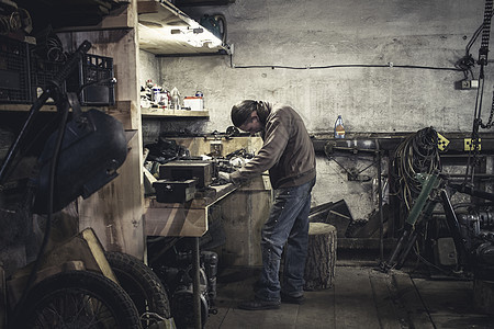 在车间维修老式摩托车轮机械的男人图片