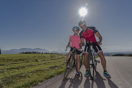 阳光照的农村公路上女孩和父亲骑自行车者的肖像图片