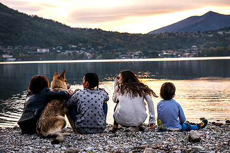 黄昏时分意大利伦巴第维尔库拉戈河边男孩与家人和狗的后视图图片
