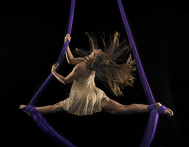 年轻女空中杂技演员用双脚在黑背景下用丝绳包着的进行分裂图片