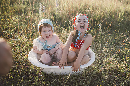 两个女孩在田野里玩水塑料浴缸图片
