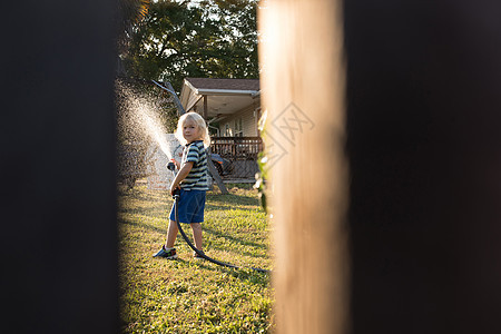 通过从水管中喷的男孩栅栏隔缝图片