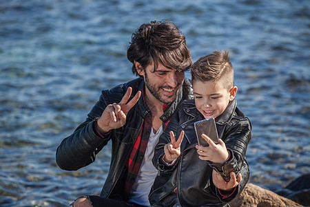 父亲和儿子在海边用智能手机自拍图片