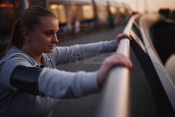 在黄昏时靠脚桥扶手对着经济的年轻女子培训图片