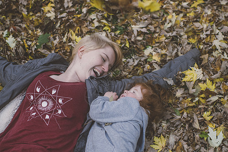 红头发女幼儿和年轻子在秋叶落时躺下图片
