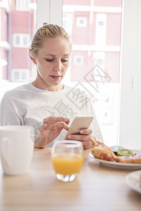 在早餐桌上使用智能电话触摸屏的年轻妇女图片