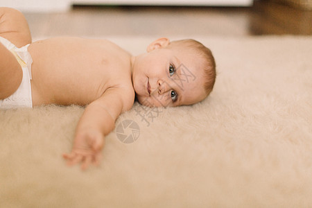 穿着尿布的可爱女婴躺在米色地毯上图片