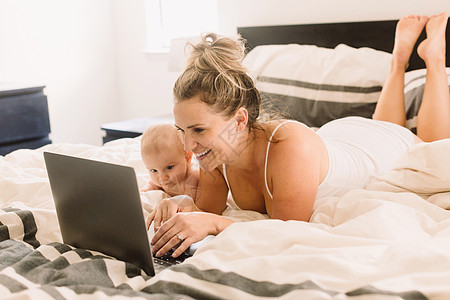 婴儿和母亲躺在床上看笔记本电脑图片