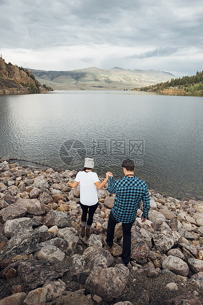 在美国科罗拉多州湖边岩石上手牵手行走的情侣图片