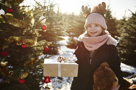 女孩手拿圣诞礼物站在圣诞树林里图片