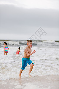 美国阿拉巴马州道芬岛海滩上沿水边跑的男孩图片