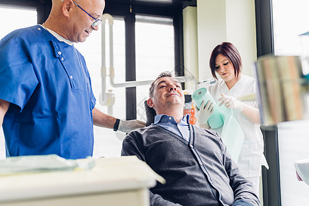 男病人坐在牙医椅子上医生站在他旁边图片