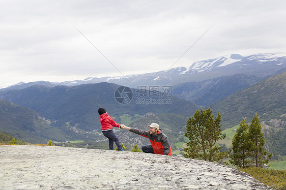 挪威奥普兰州洛美公园山地景观岩石上的男孩拽着坐在地上的父亲图片