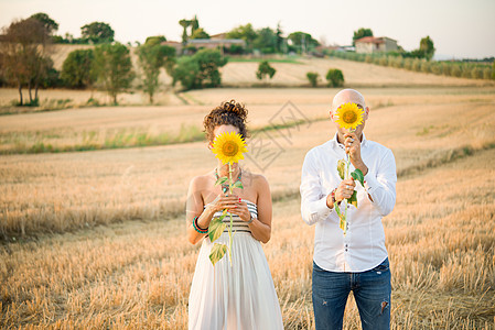 夫妻在野外将向日葵放在脸前图片