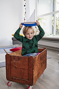 男孩坐在玩具箱中头顶着玩具船图片