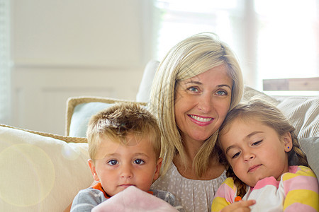 在沙发上抱着女儿和儿子的成年妇女在微笑图片